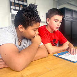 Two boys at a table, focused on a book, illustrating a moment of learning and friendship.