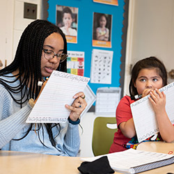 A teacher and student collaboratively writing on a piece of paper, engaged in a learning activity.