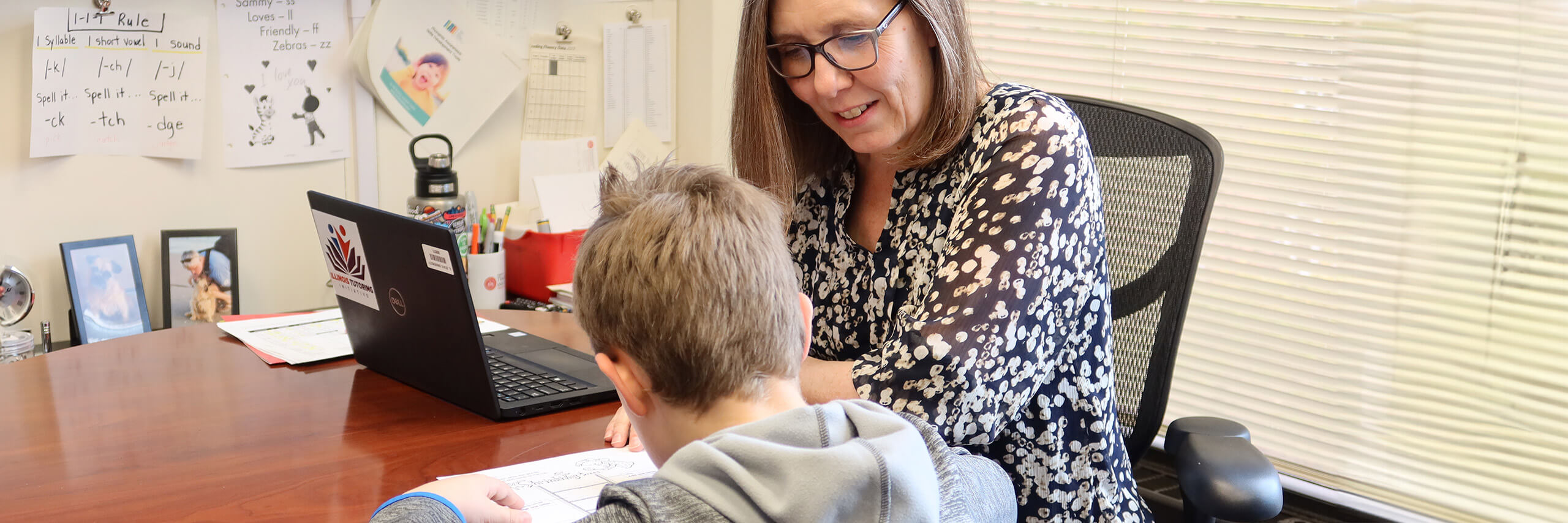 A woman and a child are at a desk with a laptop, illustrating a nurturing educational experience between them.