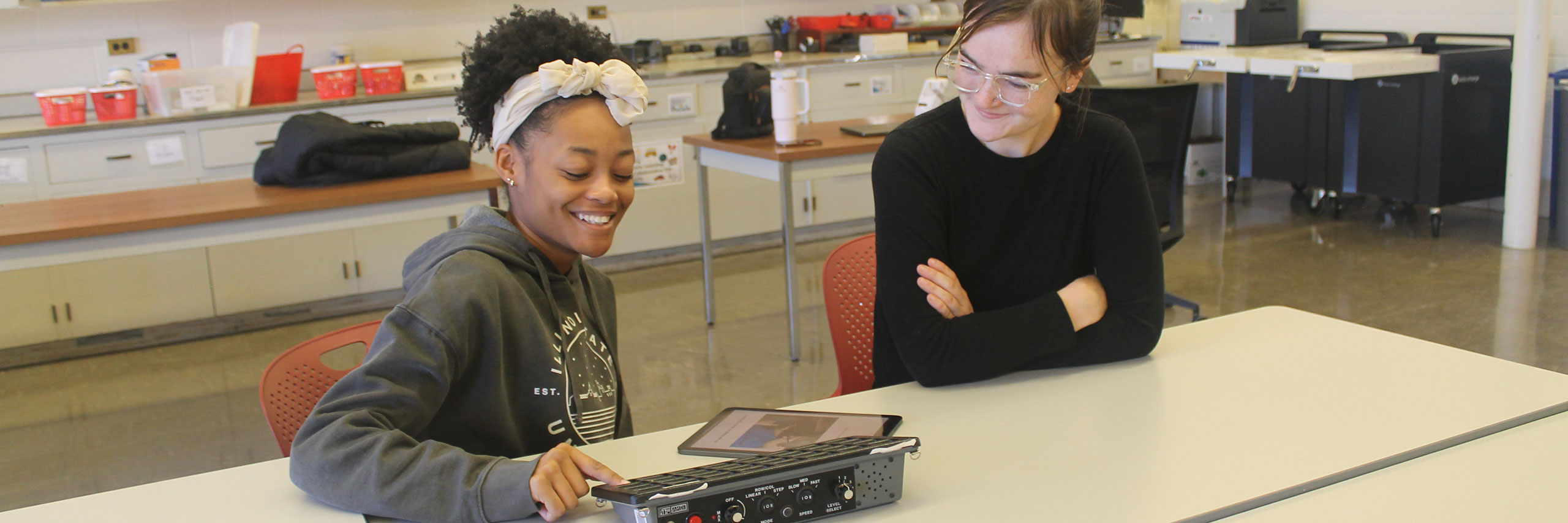 Five people standing indoors, each holding a different tactile educational tool.