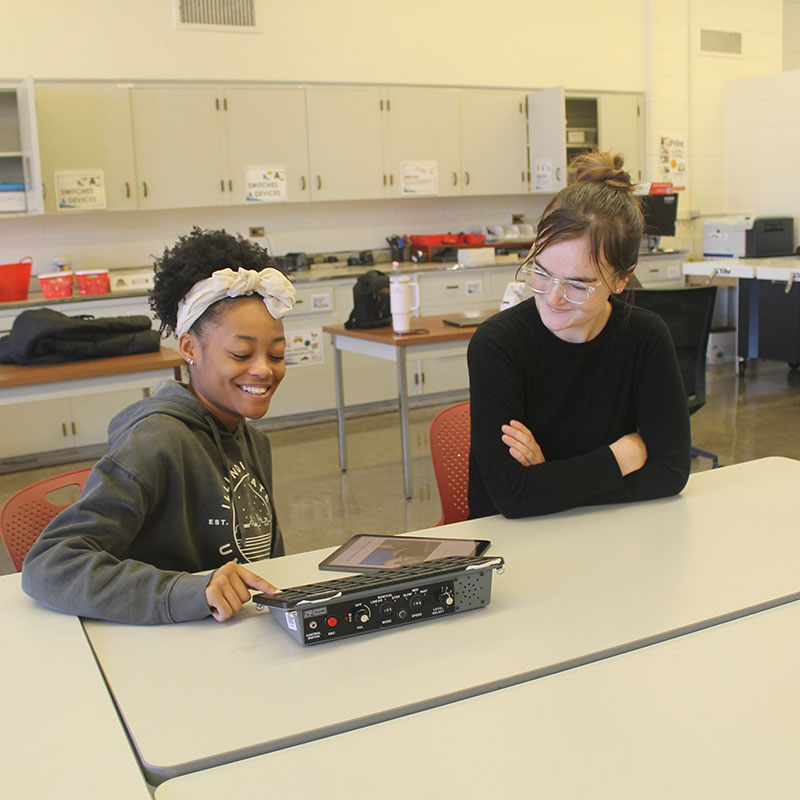 Five people standing indoors, each holding a different tactile educational tool.